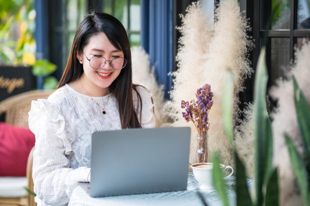 Feliz de asiáticos freelance pessoas negócios feminino casual trabalhando com um computador laptop com uma xícara de café e smartphone em uma cafeteria como o plano de fundo, o conceito de comunicação