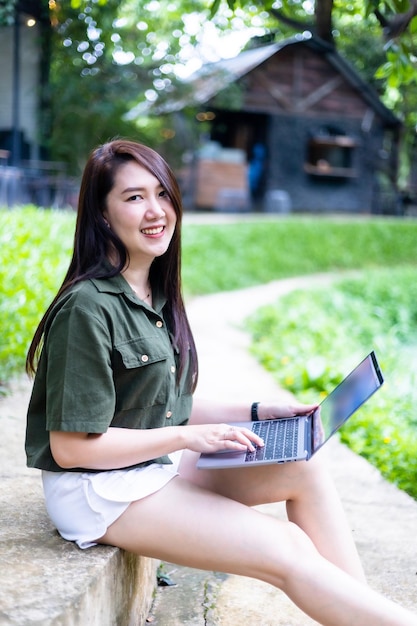 Feliz de pessoas freelance asiáticas de negócios femininos casuais trabalhando com laptop ao ar livre no dia ensolarado de verão na educação de fundo do parque e conceito de comunicação de trabalho remoto