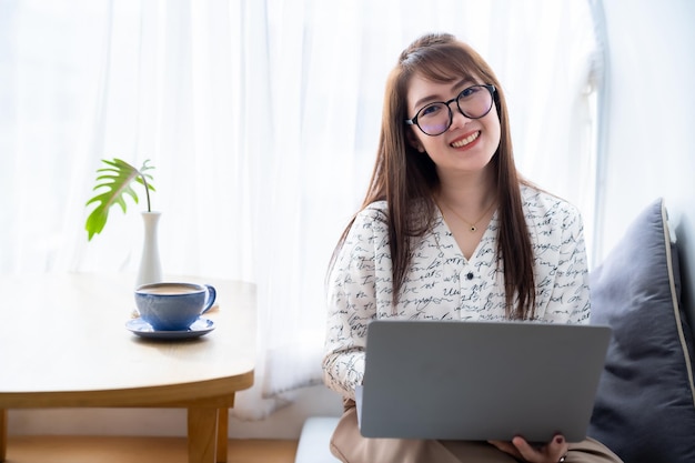 Feliz de pessoas freelance asiáticas de negócios femininos casuais trabalhando com laptop com xícara de café e smartphone no conceito de comunicação de cafeteria