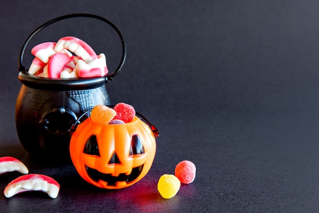 Feliz decoración de Halloween sobre fondo negro. Calabaza con caramelos de colores y caldero.