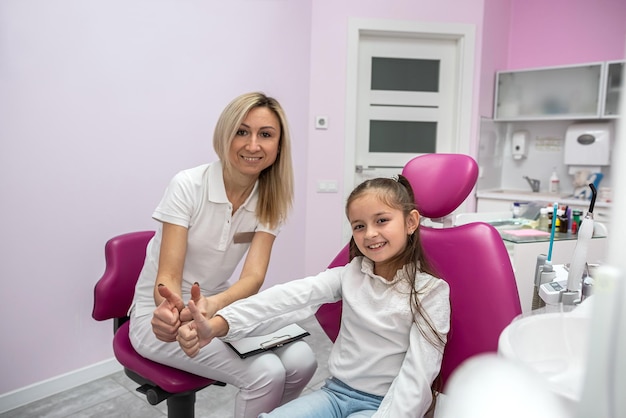 Feliz dentista feminina está entrevistando uma menina paciente no consultório de uma clínica odontológica infantil Tecnologia de tecnologia de odontologia e conceito de saúde odontologia infantil