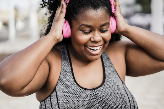 Feliz deporte mujer negra con curvas escuchando música con auriculares - Centrarse en la cara