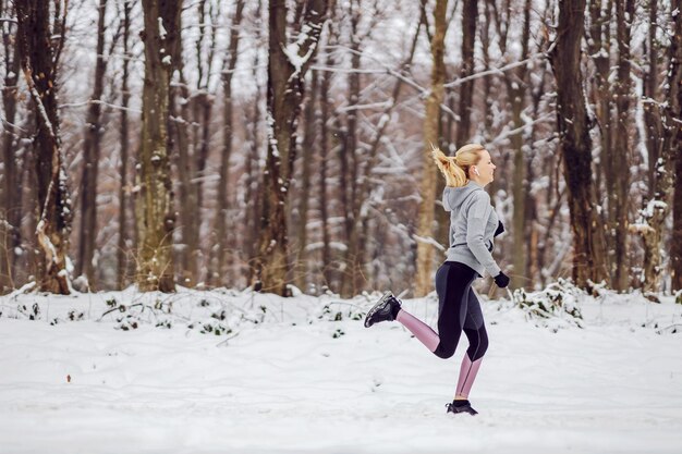 Feliz deportista en forma trotando en la naturaleza en un camino nevado en invierno