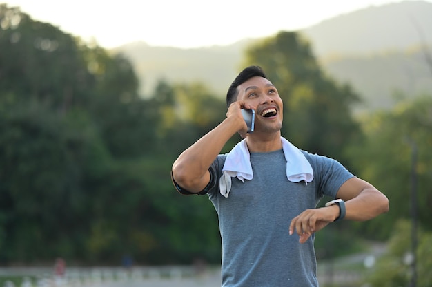 Foto un feliz deportista del milenio hablando en el teléfono móvil mientras descansa después de hacer ejercicio al atardecer