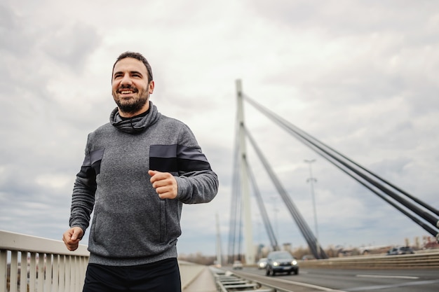 Feliz desportista correndo na ponte em tempo nublado. Conceito de estilo de vida saudável.