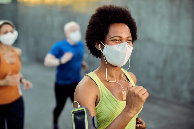 Feliz desportista negra usando máscara facial enquanto corre ao ar livre