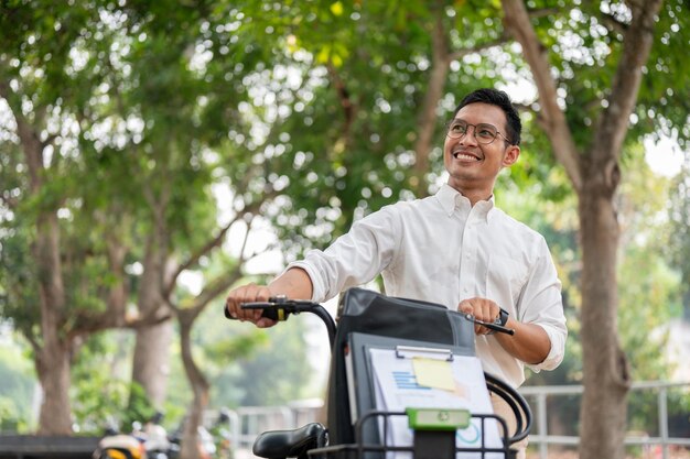 Un feliz y despreocupado hombre de negocios asiático empujando su bicicleta caminando en el parque público