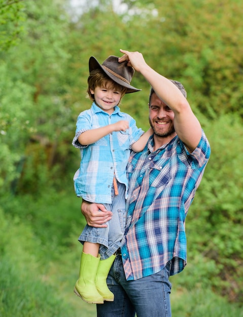 Feliz dia da terra Eco fazenda menino criança ajuda pai na agricultura pai e filho com chapéu de cowboy no rancho garoto em botas de borracha homem feliz pai na floresta humano e natureza dia da família criança com o pai