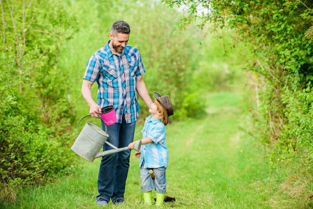 Feliz Dia da Terra. Viveiro de árvores genealógicas. Fazenda ecológica. filho pequeno ajuda o pai na agricultura. use regador e pote. Equipamento de jardim. pai e filho com chapéu de cowboy no rancho. Momento de ternura.