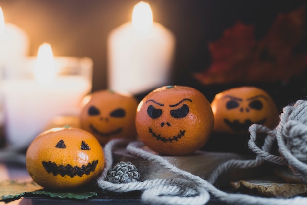 Feliz dia das bruxas cítrico, tangerinas pintadas com caras assustadoras e engraçadas. Foto escura com velas. Alternativas às abóboras tradicionais de Halloween.