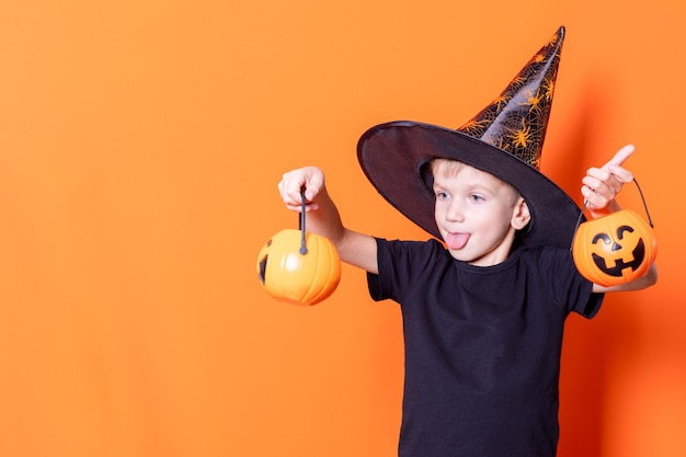 Feliz Dia das Bruxas. Crianças assustadoras de halloween. Menino assustador alegre baldes com doces na lanterna de abóbora para o halloween em fundo laranja, copie o espaço. Trick or Treat é uma tradição do Halloween.