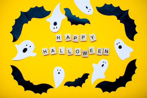 Feliz dia das bruxas e moldura feita de morcegos caseiros de papel e fantasmas de papel em um fundo amarelo brilhante