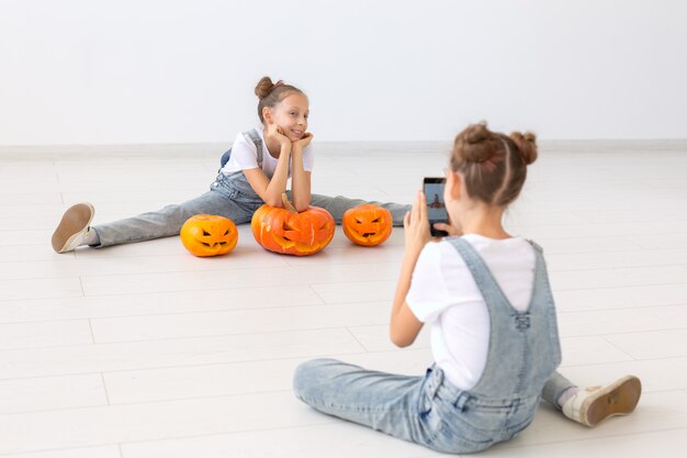 Feliz dia das bruxas, feriados e conceito de infância - meninas gêmeas gêmeas com uma lanterna de abóboras se divertindo enquanto passam o tempo dentro de casa.