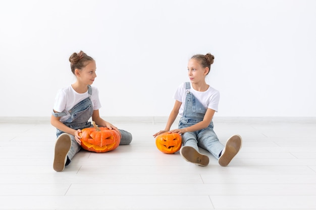 Feliz Dia das Bruxas, feriados e conceito de infância - Meninas gêmeas lindas com abóboras Jack-o'-lantern se divertindo enquanto passam o tempo dentro de casa