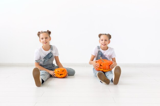 Feliz Dia das Bruxas, feriados e conceito de infância - Meninas gêmeas lindas com abóboras Jack-o'-lantern se divertindo enquanto passam o tempo dentro de casa