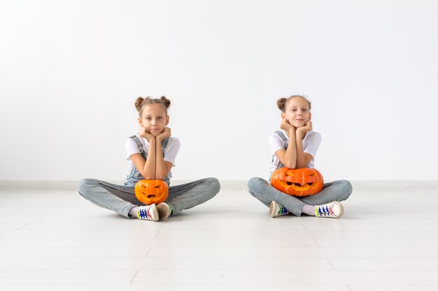 Feliz Dia das Bruxas, feriados e conceito de infância - Meninas gêmeas lindas com abóboras Jack-o'-lantern se divertindo enquanto passam o tempo dentro de casa