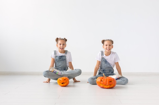 Feliz Dia das Bruxas, feriados e conceito de infância - Meninas gêmeas lindas com abóboras Jack-o'-lantern se divertindo enquanto passam o tempo dentro de casa