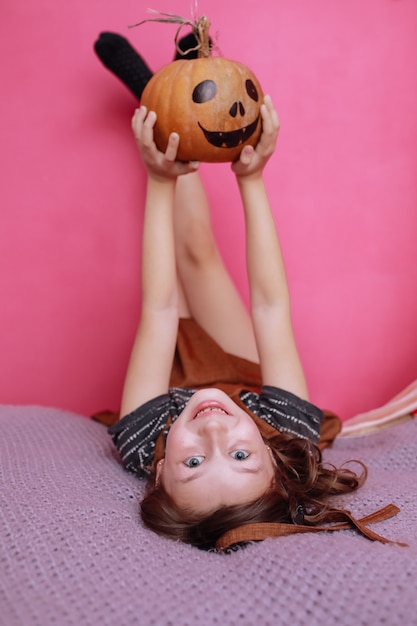 Feliz Dia das Bruxas. Menina bonitinha com fantasia de bruxa com escultura de abóbora. Família feliz se preparando para o Halloween.