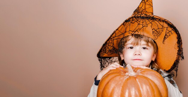 Feliz dia das bruxas menino bonitinho com chapéu de bruxa com grande abóbora jackolantern truque ou travessura espaço de cópia