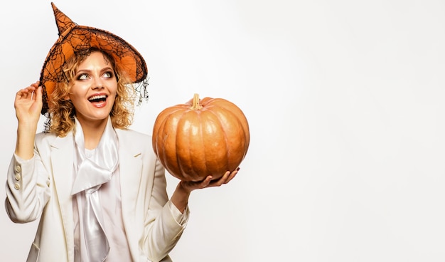 Feliz Dia das Bruxas. Mulher sorridente com chapéu de bruxa com abóbora de halloween. Doçura ou travessura. Copie o espaço para publicidade.