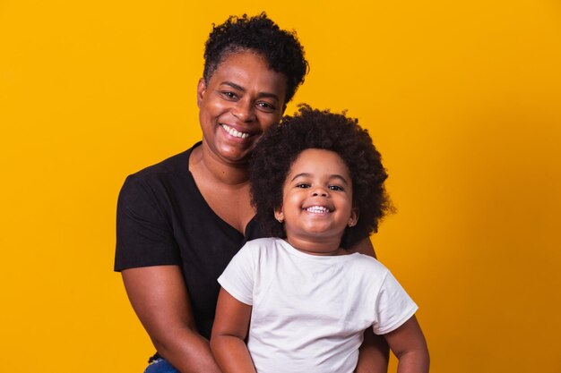 Feliz Dia das Mães! Adorável doce mãe afro-americana com filha pequena. Mãe mais velha com a filha em fundo amarelo.