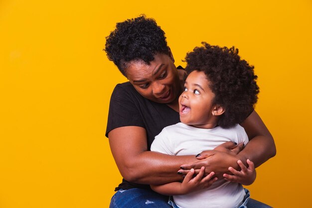 Feliz Dia das Mães! Adorável doce mãe afro-americana com filha pequena. Mãe mais velha com a filha em fundo amarelo.