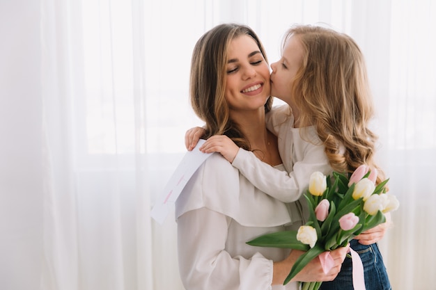 Feliz Dia das Mães. Filha criança felicita mães e dá-lhe um cartão postal e flores tulipas.