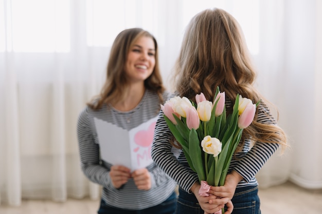 Feliz dia das mães. filha criança felicita mães e dá-lhe um cartão postal e flores tulipas.