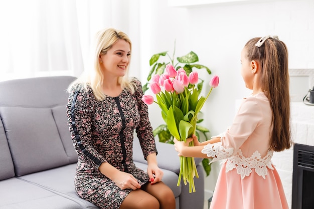 Feliz Dia das Mães. Filha criança parabeniza mães e dá flores tulipas a ela