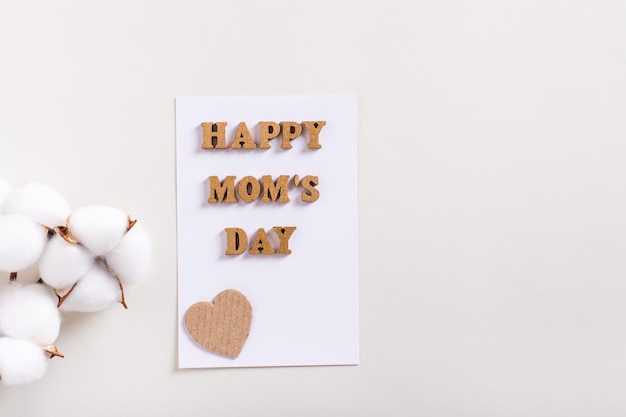Feliz dia das mães Uma folha de papel com letras e um ramo de algodão sobre fundo claro