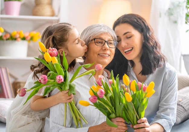 Feliz dia das mulheres Filha criança está parabenizando mamãe e vovó dando-lhes flores tulipas Vovó mamãe e menina sorrindo e abraçando Férias em família e união