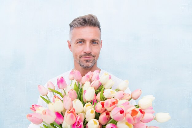 Feliz dia das mulheres. para alguém especial. homem com buquê de tulipas. cara bonito segurando flores cor de rosa. homem atraente com flores. homem carrega um presente para o dia dos namorados ou a festa de aniversário. loja de flores.