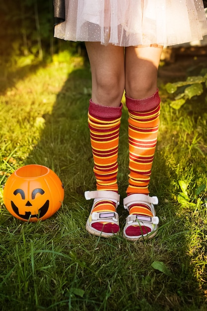 Feliz dia de halloween a criança está de pé na grama em uma fantasia de bruxa perto da abóbora jack