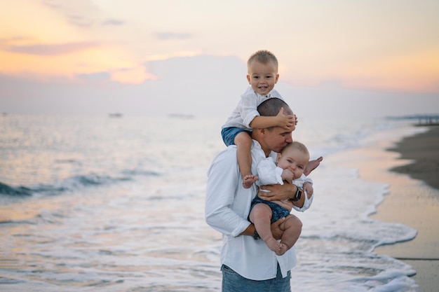 Feliz dia dos pais Pai e filhos brincam na praia Pai e ele Filhos juntos curtindo o pôr do sol Pai solteiro amoroso abraça dois filhinhos fofos