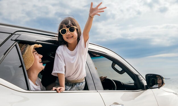 Feliz día familiar madre asiática padre e hijos sonriendo sentados en un coche blanco compacto mirando por las ventanas verano en la playa seguro de coche vacaciones familiares viajes concepto de viaje por carretera