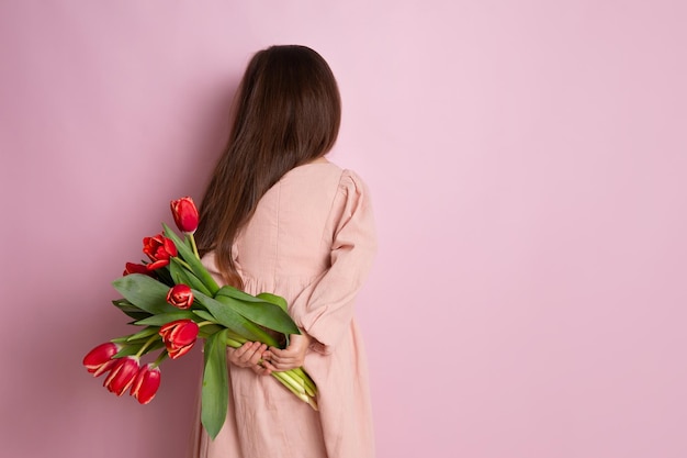 Feliz Dia Internacional da Mulher Uma linda garota segura um buquê de tulipas vermelhas nas costas Rosa