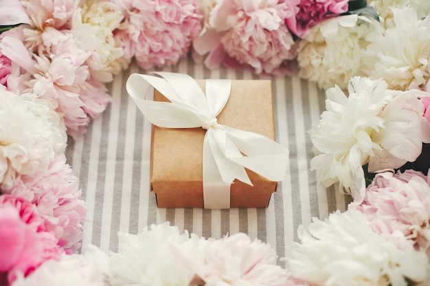 Feliz día de la madre Día internacional de la mujer Regalo de cumpleaños Hermosa caja de regalo con cinta en marco de peonías rosas y blancas en la mesa Saludos de temporada