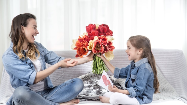 Feliz día de la madre. Dulce hijita con un gran ramo de tulipanes felicita a su madre. En el interior de la sala de estar, el concepto de una vida familiar feliz.