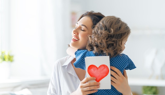 ¡Feliz día de la madre! La hija del niño está felicitando a mamá y dándole una postal. Mamá y niña sonriendo y abrazándose. Vacaciones familiares y unión.