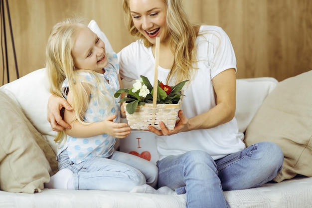 ¡Feliz dia de LA MADRE! La hija del niño felicita a mamá y le da una canasta de flores de primavera. Conceptos de familia e infancia.