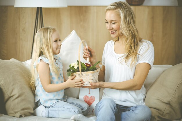 Feliz dia de LA MADRE. La hija del niño felicita a mamá y le da una canasta de flores de primavera y una postal con un dibujo del corazón. Conceptos de familia e infancia.