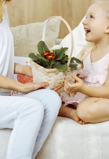 ¡Feliz dia de LA MADRE! La hija del niño felicita a mamá y le da una canasta de flores de primavera y una postal con un dibujo del corazón. Conceptos de familia e infancia.