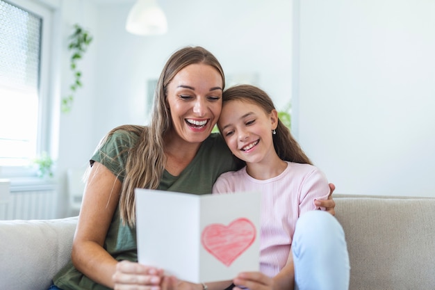 ¡Feliz día de la madre! La hija del niño felicita a mamá y le da una postal. Mamá y niña sonriendo y abrazándose. Vacaciones familiares y convivencia.