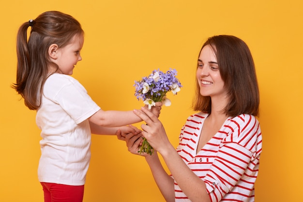 ¡Feliz día de la madre! La hija del niño felicita a mamá y le da su ramo de flores.