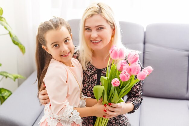 Feliz día de la madre. La hija del niño felicita a mamá y le regala tulipanes de flores. Mamá y niña sonriendo y abrazándose. Vacaciones familiares y convivencia.