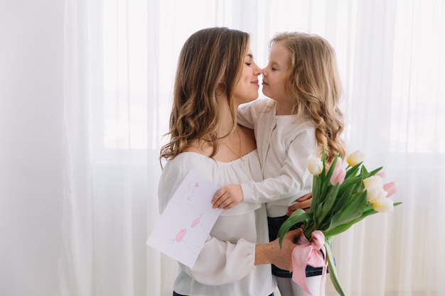 Feliz día de la madre. La hija del niño felicita a las mamás y le regala una postal y flores de tulipanes.