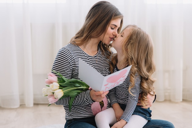 Feliz día de la madre. La hija del niño felicita a las mamás y le regala una postal y flores de tulipanes.