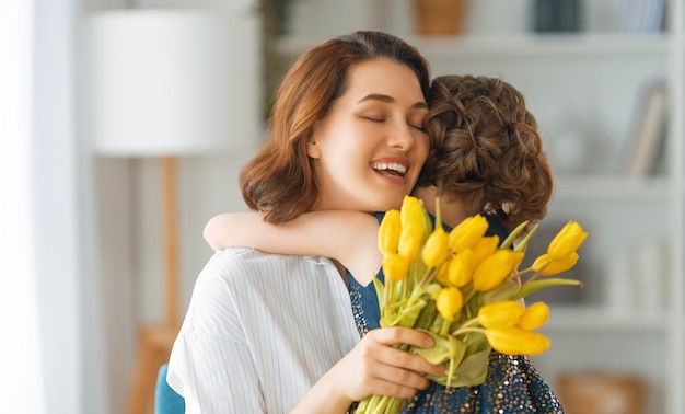 Feliz día de la madre Niño hija felicitando a mamá y dándole flores