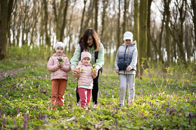 Feliz Día de la Madre Te amamos mamá Madre con un ramo de flores y tres niños en el bosque floreciente de primavera