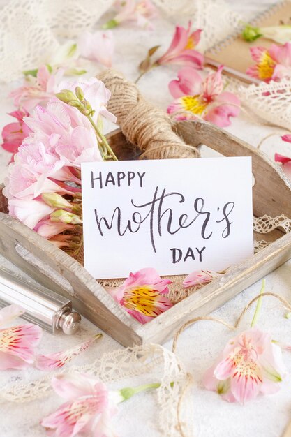 Feliz día de las madres tarjeta escrita a mano en una bandeja de madera entre flores rosadas de cerca